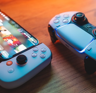 A gaming scenario featuring a smartphone with a game interface next to two controllers on a wooden surface. The smartphone displays vibrant images and icons, while the controllers feature a sleek, modern design with buttons and joysticks prominently visible. Warm lighting enhances the scene.